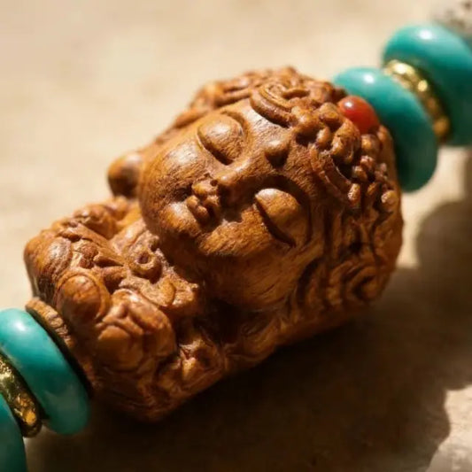Close-up of a handcrafted Tibetan-style carved wooden Buddha head bead with turquoise spacer beads, detailed texture and spiritual jewelry design.