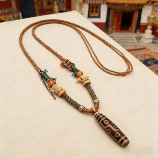Handmade Tibetan style Dzi bead necklace with braided cord, wooden beads and ethnic details, flat lay on neutral background