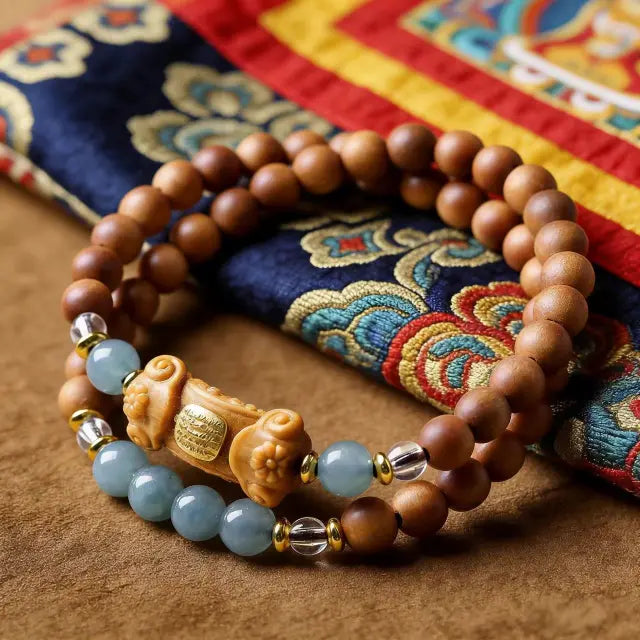 Handmade Tibetan bracelet with wooden beads, jade stones, and decorative centerpiece placed on traditional patterned fabric
