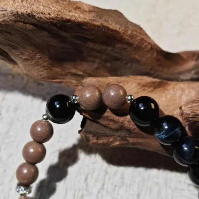 A handmade bracelet featuring natural wood beads and black onyx stones, styled on a rustic wooden background for a minimalist look