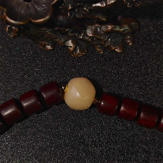 A handmade rosewood double wrap bracelet, designed for spiritual grounding and attracting abundance. Features two natural wood strands with a minimalist brass charm, shown on a textured neutral background.