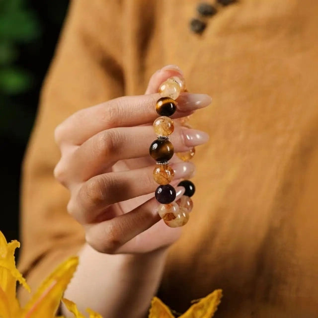 A woman holding a natural rutilated quartz and tiger's eye beaded crystal bracelet, showcasing the stone layout against a linen outfit.
