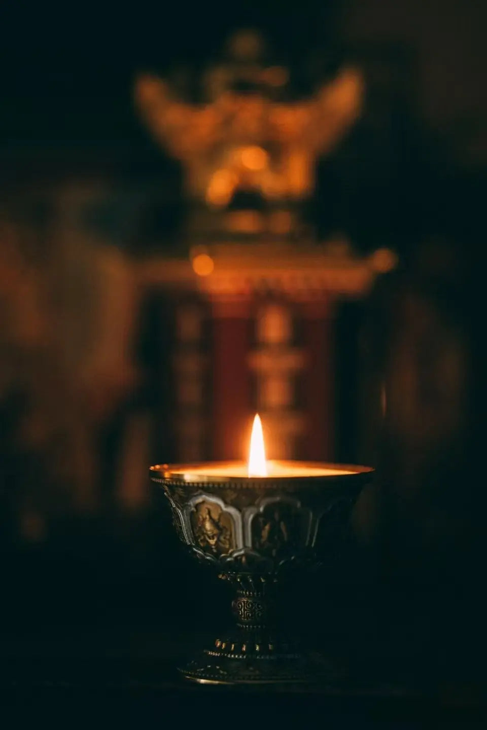 A handcrafted Tibetan brass butter lamp with a warm candle flame, creating a peaceful meditation altar atmosphere
