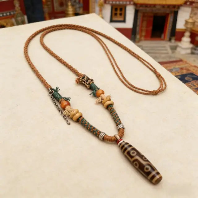 Handmade Tibetan style Dzi bead necklace with braided cord, wooden beads and ethnic details, flat lay on neutral background