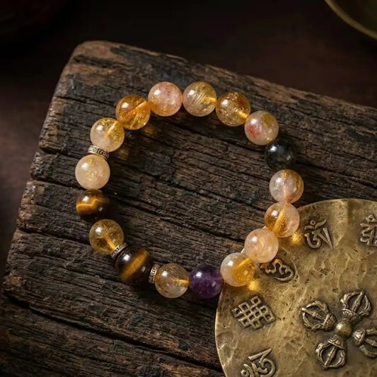 A feng shui multi-gemstone healing bracelet laid flat on a rustic wooden surface next to a traditional brass Tibetan Buddhist amulet disk.