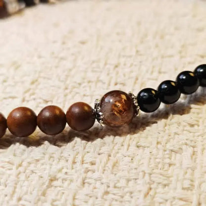 A handcrafted bracelet featuring natural wood beads, black onyx stones, and a warm amber center bead for a balanced and minimalist style